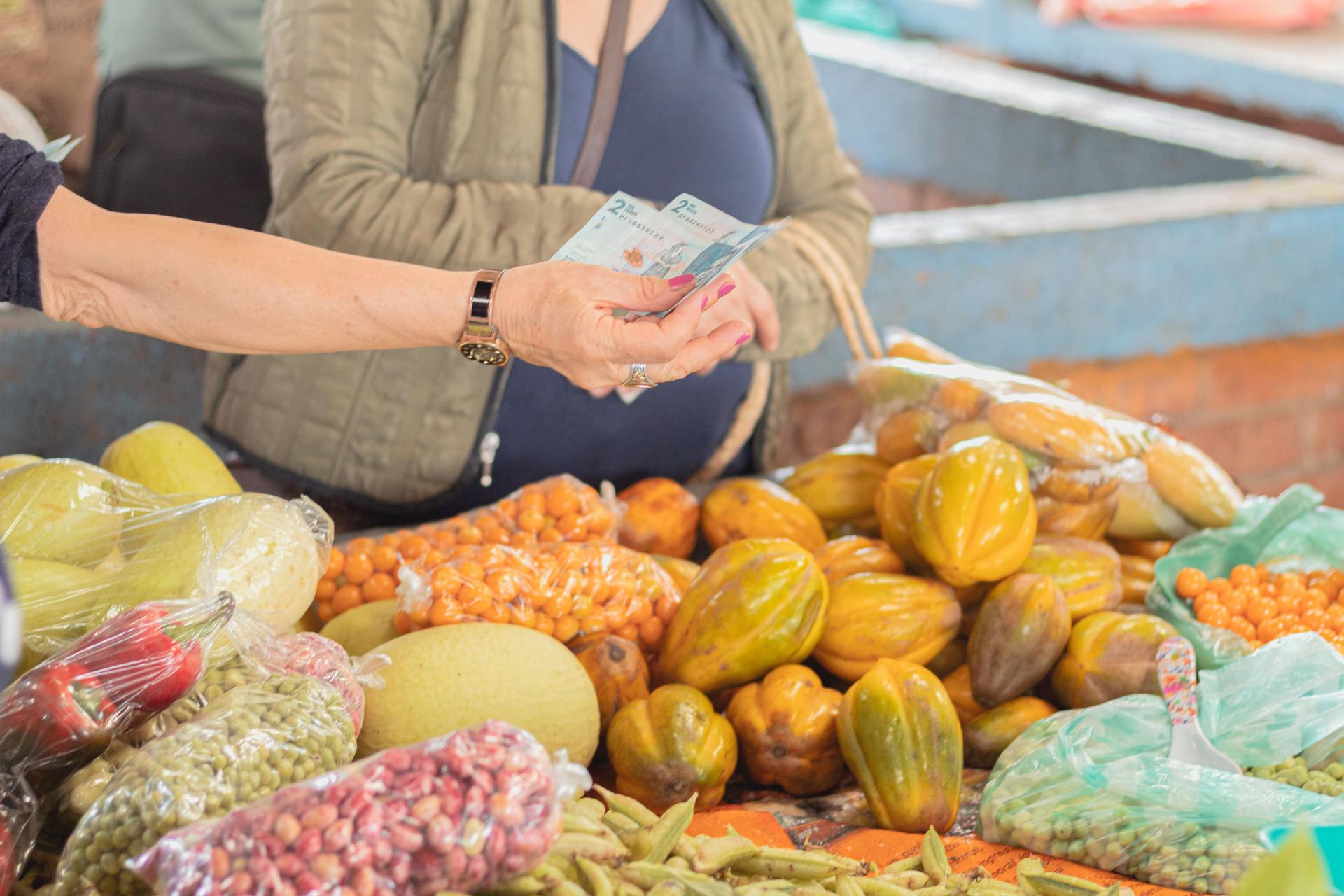 Mujeres comprando en el mercado de agricultores. Puesto del mercado local lleno de frutas y granos frescos envasados. Compra de productos agrícolas. Dinero colombiano. Concepto de oferta y demanda.